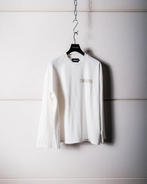 White long-sleeve shirt hanging on a hook against a light-colored wall.